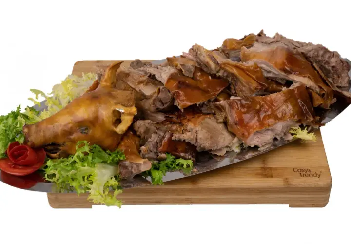 Un cochon de lait entier, rôti à la perfection, est servi sur un plateau avec de la laitue et une rose en tomate. La cuisson du cochon de lait est impressionnante.