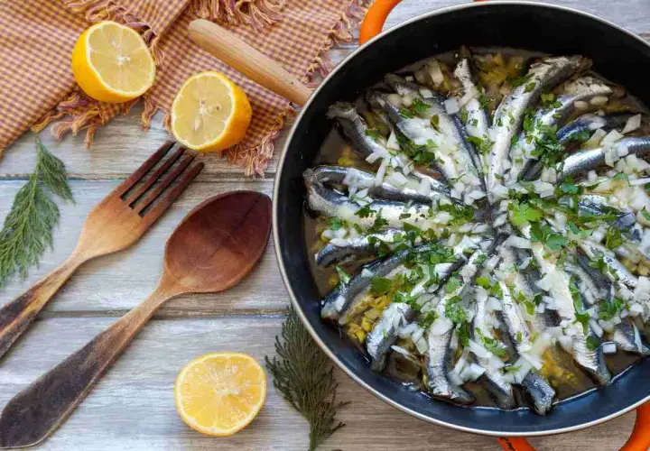 Alici in padella, pronte per essere gustate, con limone, erbe aromatiche e cipolla. Un piatto semplice e saporito.