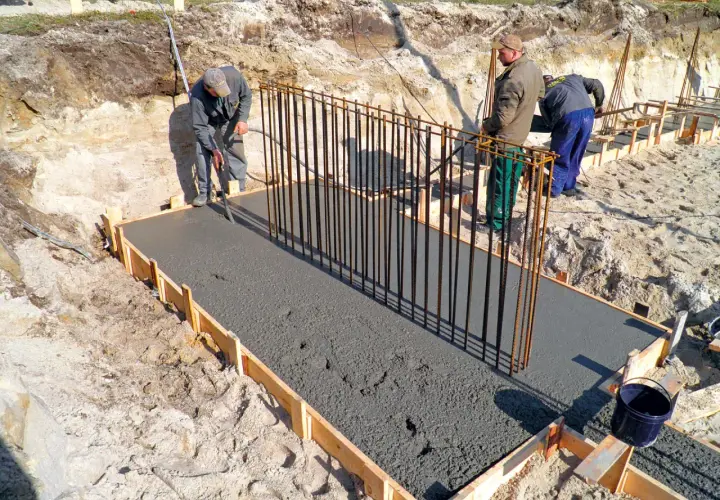 Budowa fundamentów: pracownicy wylewają beton na zbrojenie, tworząc solidny żelbeton.