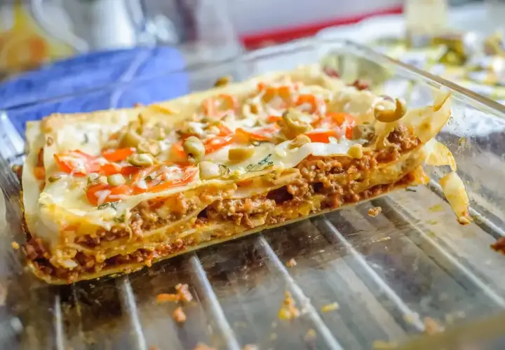Pyszne, domowe piec lasagne z warstwami mięsa mielonego, makaronu i sera, ozdobione pomidorami i oliwkami.