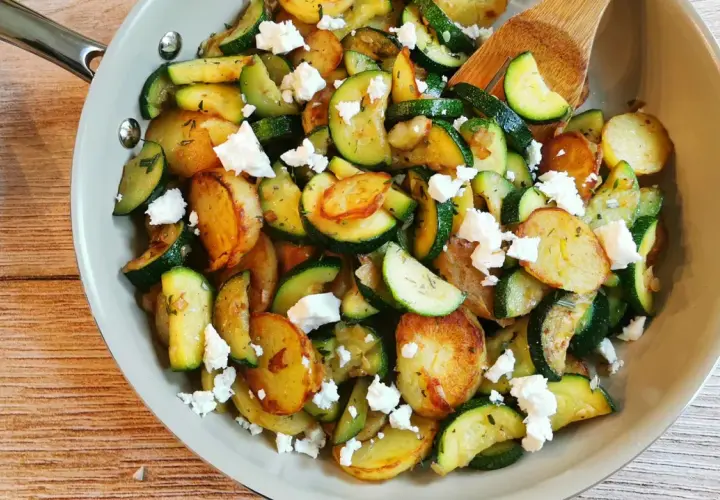 Herzhafte zucchini pfanne mit goldbraunen Kartoffelscheiben und zerbröseltem Feta, garniert mit frischen Kräutern.