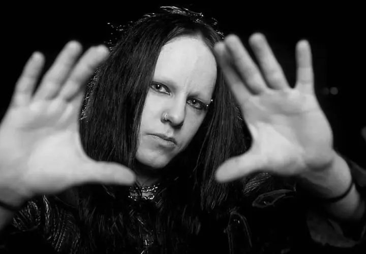 Joey Jordison, perkusista zespołu Slipknot, z rękami przed twarzą, w czerni i bieli.