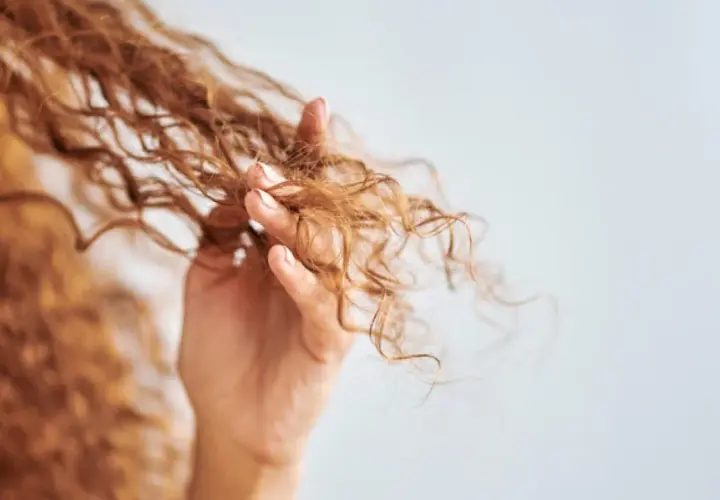 Mano acariciando cabello rizado, mostrando cómo rizar el pelo con espuma para definir ondas.
