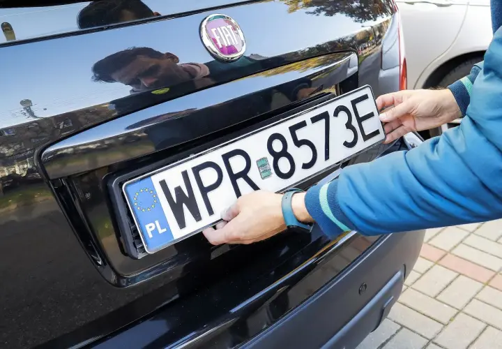 Ręce montują tablicę rejestracyjną. Uniknięcie mandatu za brak tablicy rejestracyjnej jest ważne.