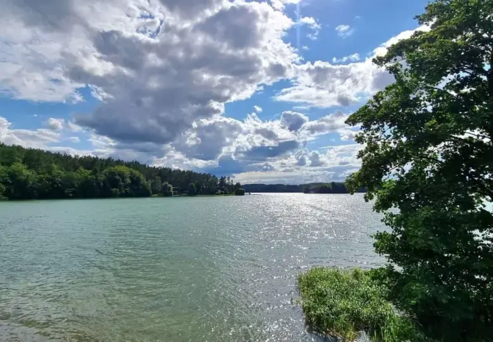Spokojne jezioro na Kaszubach, otoczone lasem, z chmurami na niebie. To jak brama kaszubska do natury.