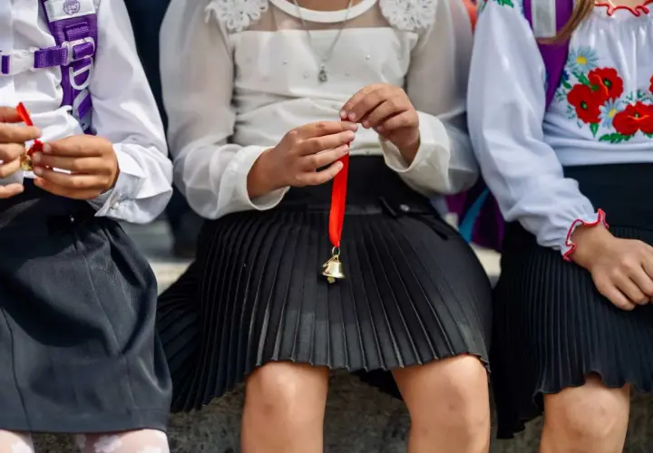 Dzieci w szkolnych strojach, jedno trzyma dzwoneczek na czerwonej wstążce. Od jakiej średniej jest pasek?
