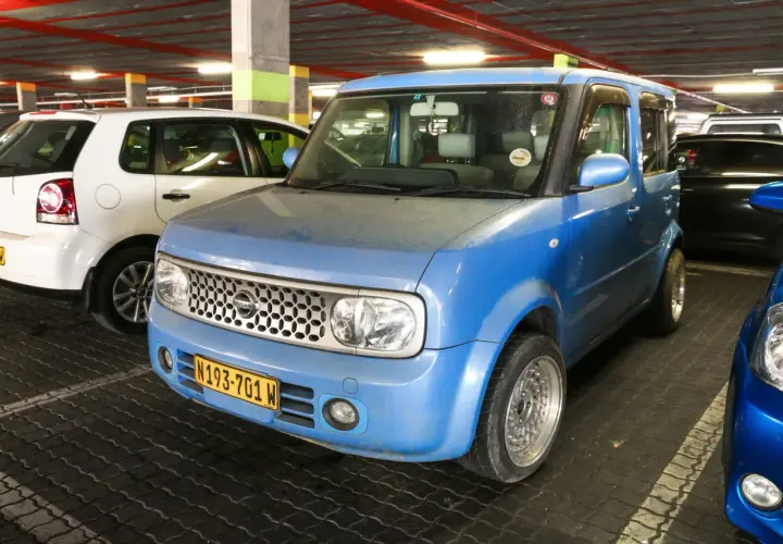 Niebieski Nissan Cube z tablicą rejestracyjną N193-701 W zaparkowany obok białego Volkswagena.