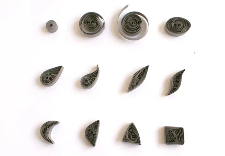 Różne kształty z papieru, pokazujące, quilling co to jest. Kółka, łezki, listki, księżyce, trójkąty i kwadraty.