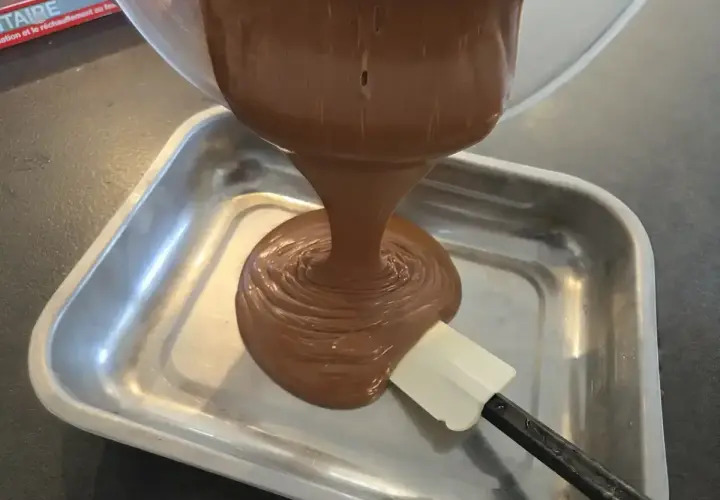 Une ganache au chocolat, inspirée par le Toblerone, est versée dans un plat métallique. Une spatule aide à l'étaler.
