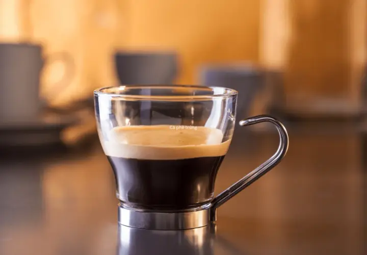 Kawa ristretto w szklanej filiżance z metalowym uchem. Kremowa pianka na ciemnym espresso.