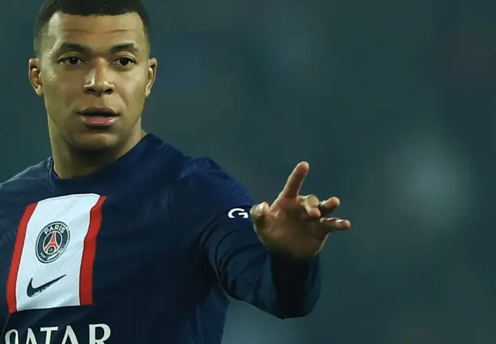 Kylian Mbappé w koszulce PSG, gdzie gra, pokazuje gest dłonią.