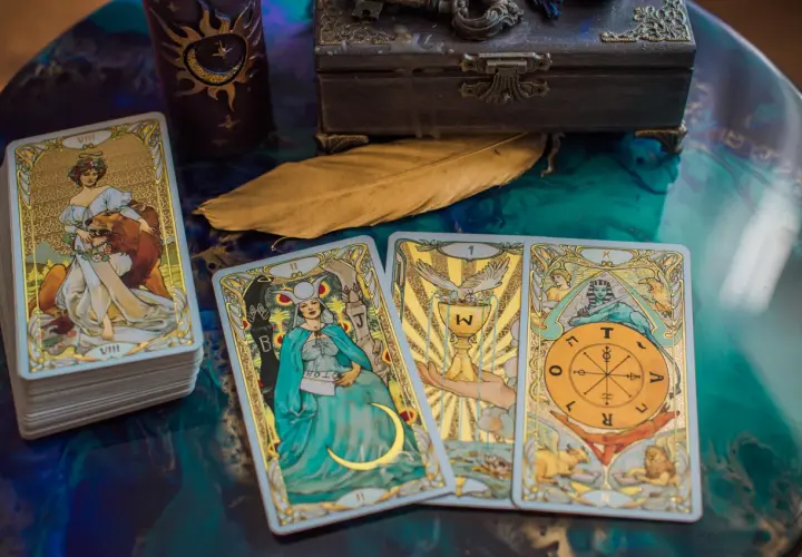 Tarot byk miesięczny: talia kart z wizerunkami postaci i symboli, w tym karta z bykiem, świeca, skrzynia i pióro.