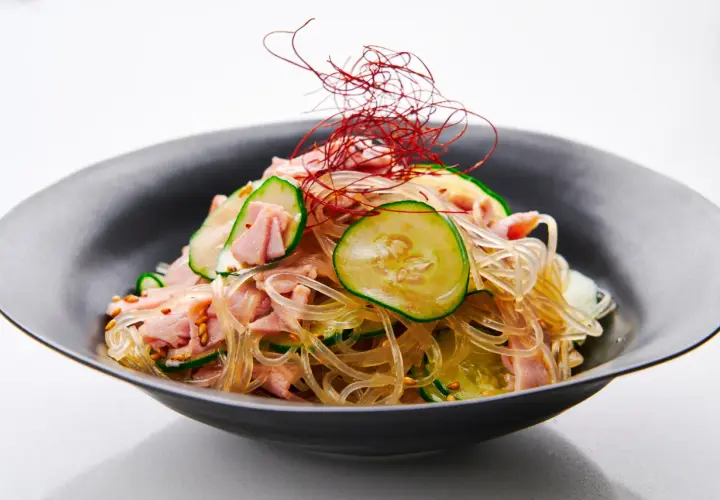 A refreshing harusame salad with glass noodles, sliced cucumber, and ham, garnished with delicate red chili threads.