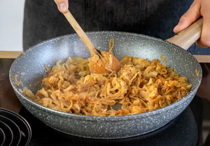 Omas Zwiebelrostbraten wird in der Pfanne zubereitet. Zwiebeln werden goldbraun gebraten, ein köstlicher Duft liegt in der Luft.