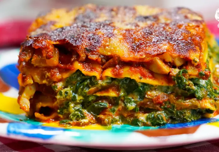 Porción de lasaña de verduras, con capas de pasta, espinacas y salsa roja, servida en un plato colorido.