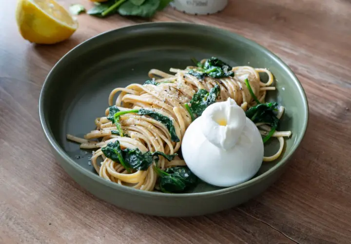 Zitronen Pasta mit Spinat und Burrata auf einem grünen Teller, daneben eine Zitronenhälfte.