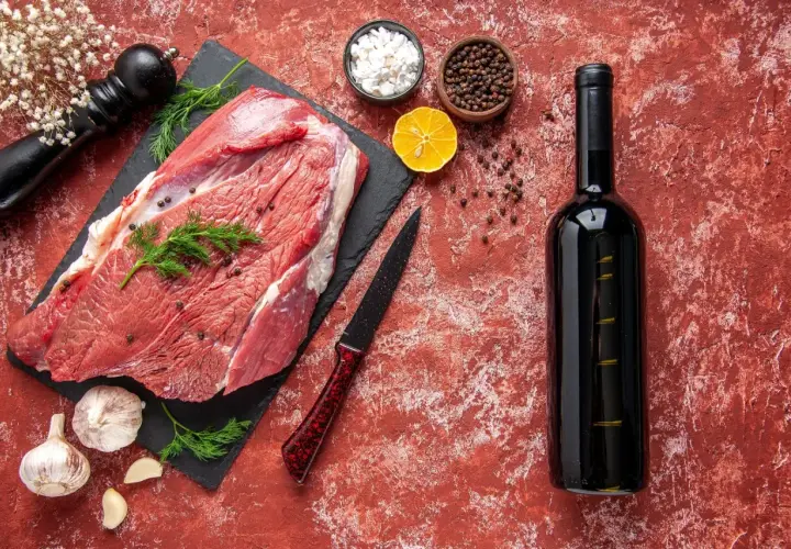 Un morceau de viande crue, prêt pour un repas savoureux avec un vin rouge. Des épices, de l'ail et une tranche de citron complètent la scène.