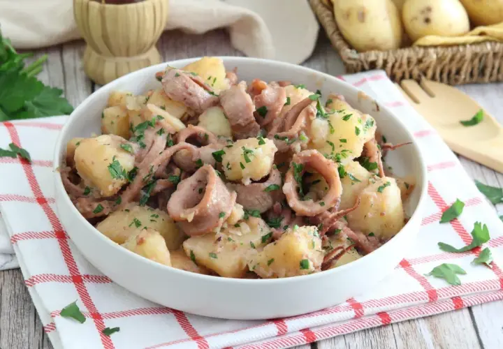 Un saporito piatto di totani e patate, condito con prezzemolo fresco, servito in una ciotola bianca su un tovagliolo a quadri rossi.