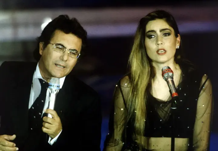 Al Bano i jego nowa partnerka na scenie, w blasku świateł, śpiewają do mikrofonów.