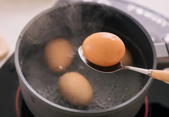 Une cuillère sort un œuf à la coque de l'eau bouillante. Trois autres œufs sont dans la casserole.