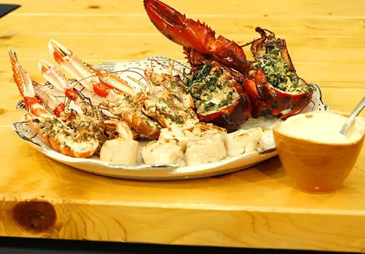 En tallrik med grillade skaldjur, inklusive hummer och havskräftor, serveras med en skål dippsås.