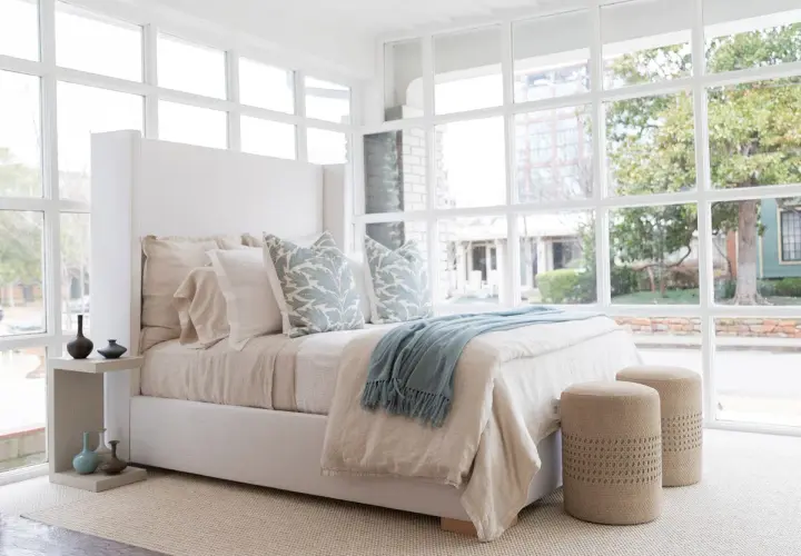 A light blue throw with fringe adds a cozy touch to this serene bedroom, draped over a bed with linen bedding.