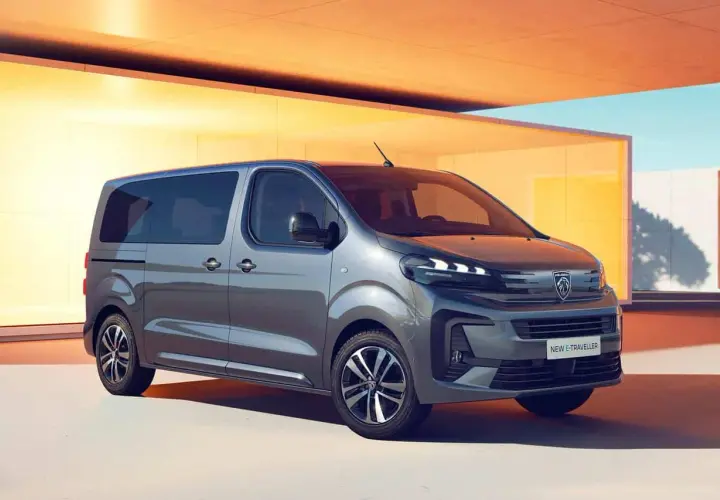 Nowy Peugeot e-Traveller, szary van, zaparkowany przed nowoczesnym budynkiem z żółtymi akcentami.