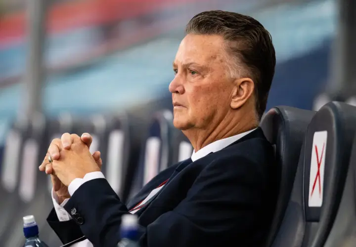 Louis van Gaal, znany z prowadzenia drużyny z pasją, siedzi z zamyślonym wyrazem twarzy, dłonie splecione.