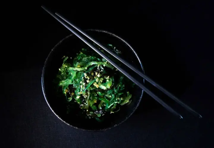 Insalata di wakame, un piatto ricco di **wakame proprietà** benefiche, guarnita con semi di sesamo e cipollotto, pronta per essere gustata con le bacchette.