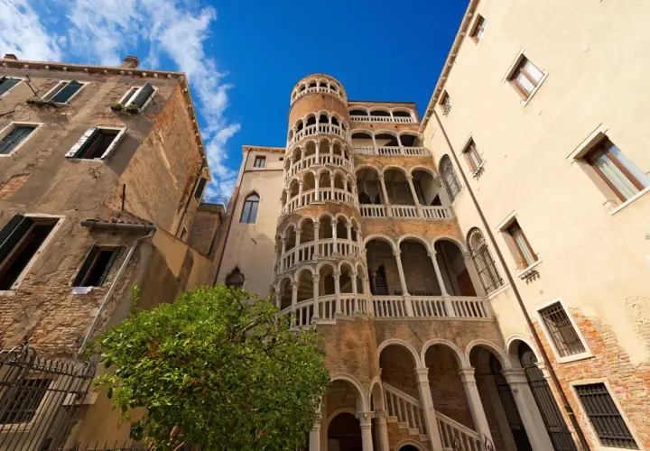 Le célèbre escalier en colimaçon du Bovolo à Venise, une merveille architecturale médiévale, se dresse fièrement sous un ciel bleu éclatant.