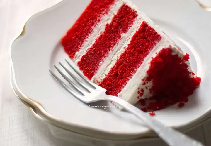 Una fetta di torta Red Velvet, con strati rossi e crema bianca, pronta per essere gustata. La ricetta perfetta per un dolce indimenticabile.