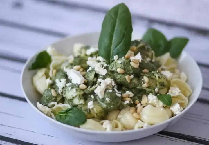 Pyszny makaron z fetą, polany zielonym pesto i posypany orzeszkami pinii. Idealny na szybki obiad.