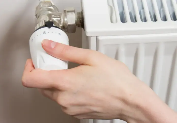 Mano girando la perilla del radiador hacia la izquierda para cerrarlo.