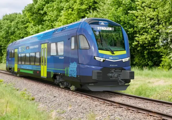 Niebieski pociąg Stadler RSZERO na wodór jedzie po torach wśród zieleni.