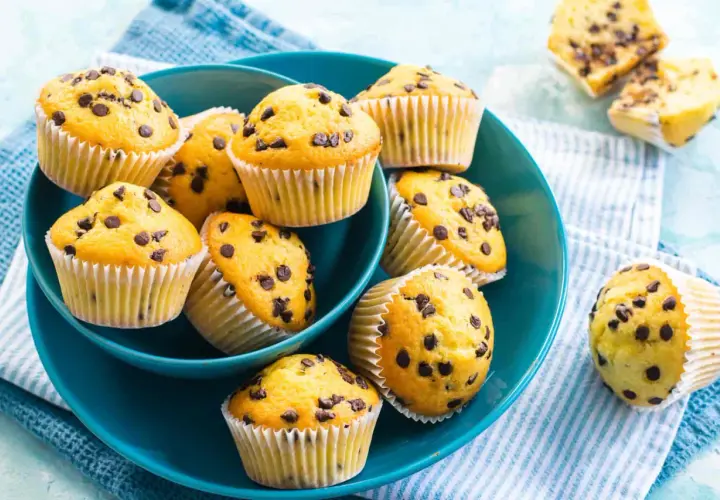 Muffin con gocce di cioccolato, dorati e invitanti, serviti in una ciotola blu. Perfetti per una pausa golosa.