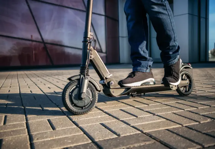 Osoba na hulajnodze elektrycznej jedzie po chodniku. Czy hulajnogą można jeździć po ścieżce rowerowej? To zależy od przepisów.