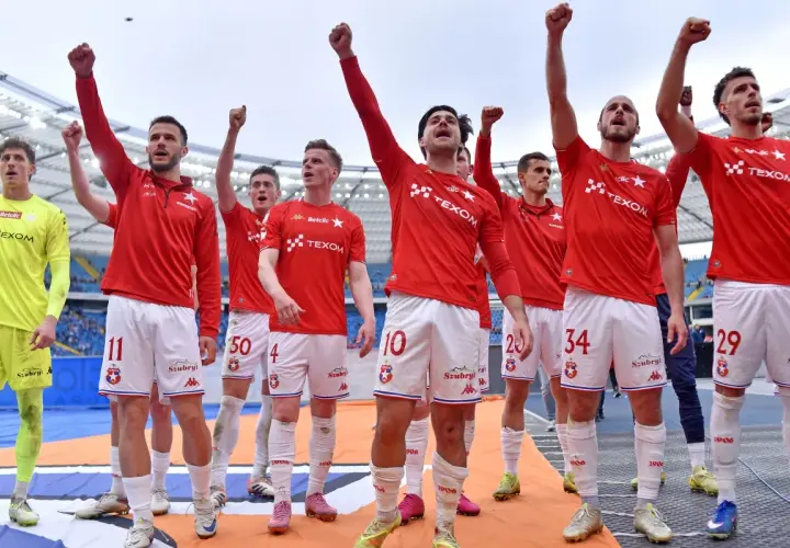 Piłkarze Wisły Kraków świętują, podnosząc ręce w geście triumfu. Ich stroje sugerują, że to ważny moment, być może związany z udanymi transferami.