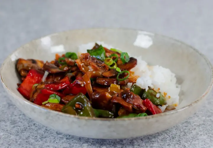 En skål med ris och en smakrik kyckling cashew-röra med paprika, champinjoner och salladslök.