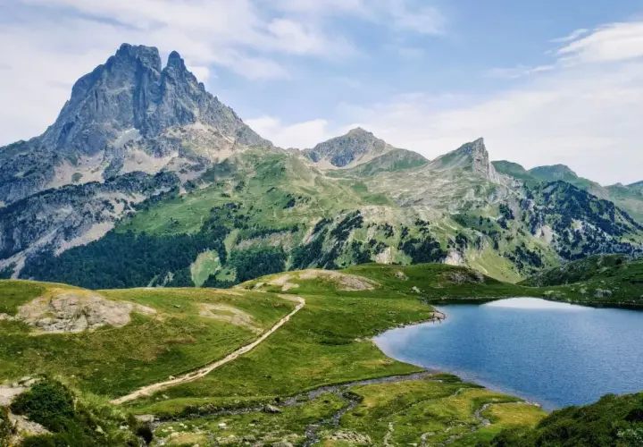 Majestuoso pico en el valle de Ossau, con un lago azul y senderos serpenteantes entre verdes colinas.