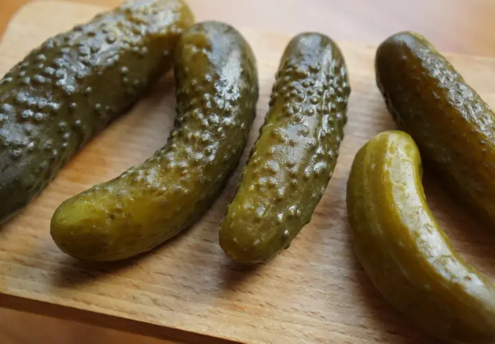 Kilka ogórków kiszonych leżących na drewnianej desce.