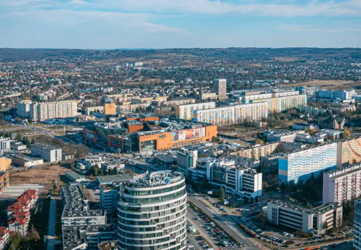 Widok na Rzeszów z lotu ptaka. Widać nowoczesne budynki, centrum handlowe i osiedla mieszkaniowe. Ceny mieszkań Rzeszów są tu widoczne w kontekście rozwoju miasta.