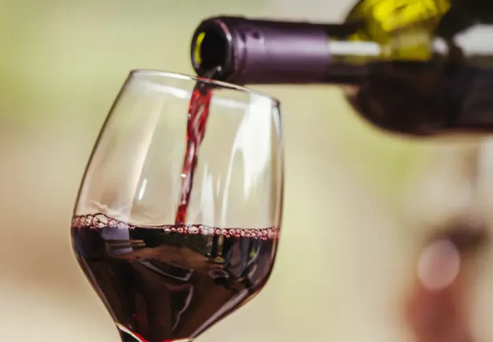Czerwone wino nalewane do kieliszka. Widoczne "łzy" na ściance, świadczące o zawartości alkoholu.