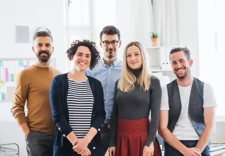 Fünf lächelnde Personen stehen im Büro. Sie haben erfolgreich ihr Fernstudium anerkannt und feiern ihren Erfolg.