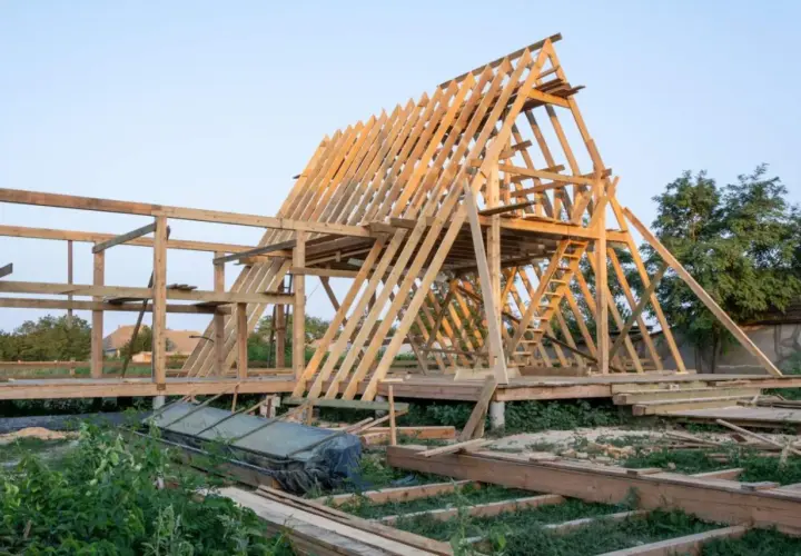 Drewniana konstrukcja domku letniskowego w budowie. Widać szkielet dachu i ścian, a także elementy, które mogą stanowić jaki fundament pod domek letniskowy drewniany.