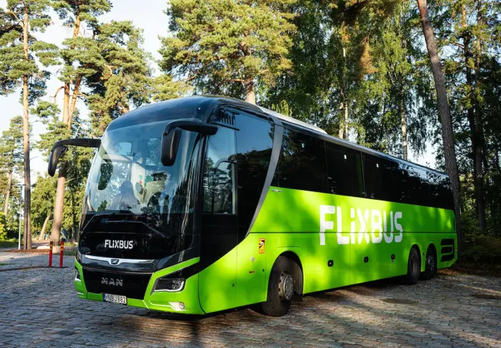 Zielony autokar Flixbus zaparkowany na brukowanym placu, otoczony drzewami.