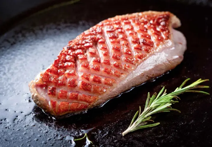 Magret de canard à la poêle, peau dorée et croustillante, avec une branche de romarin. Le temps de cuisson est idéal pour un plat savoureux.