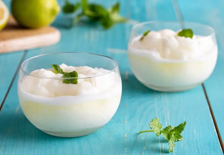 Due bicchieri di sorbetto al limone senza albume, guarniti con menta fresca, su un tavolo di legno blu.