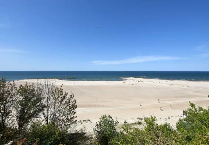 Szeroka, piaszczysta plaża w Jarosławcu, z łagodnymi falami Bałtyku i zielenią w tle. Idealne miejsce na relaks i podziwianie widoków, oferujące liczne atrakcje.