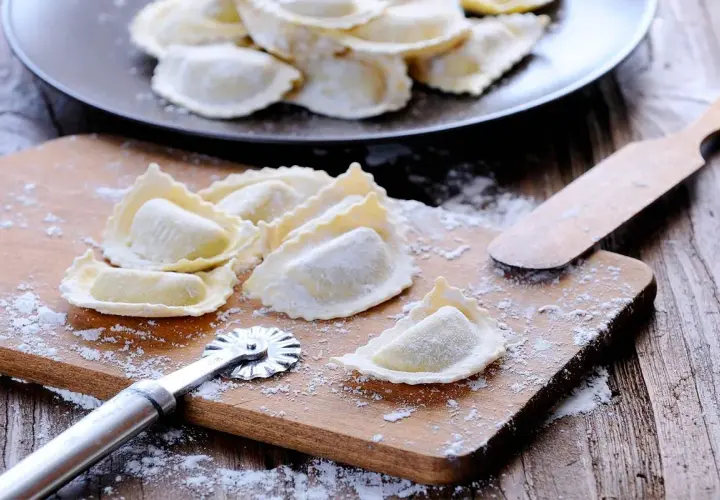 Raviolis frais sur une planche à découper avec une roulette à pâtisserie et une spatule.