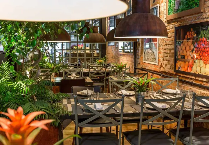 Tavoli apparecchiati in un ristorante con piante rigogliose e foto di frutta. Un'ottima opzione per sapere dove mangiare a Madrid.